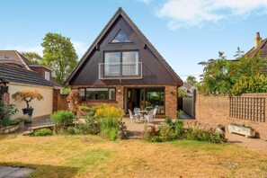 A two-story house with a balcony, a patio with outdoor furniture, and a well-maintained garden. - 3 Bed in Christchurch (oc-m45917) (Christchurch)