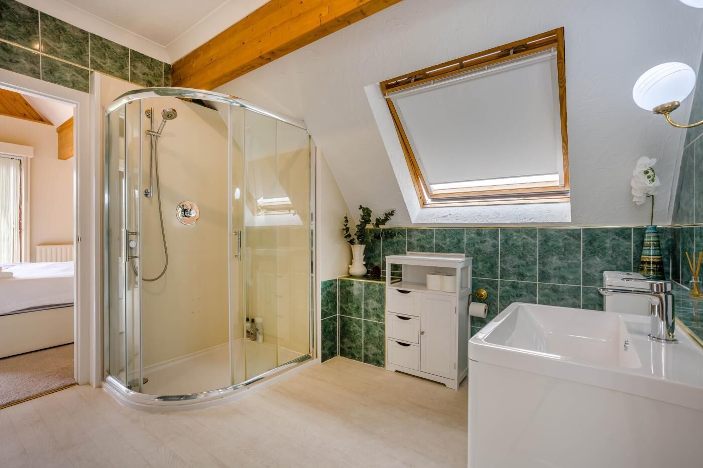 Un baño moderno con cabina de ducha de vidrio, tocador blanco y tragaluz sobre el espejo.