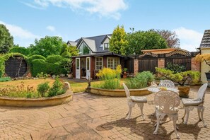 A patio area with outdoor seating, a garden, and a house with a sloped roof. - 3 Bed in Christchurch (oc-m45917) (Christchurch)