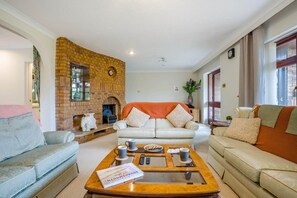 Ein Wohnzimmer mit Kamin aus Backsteinen, zwei Sofas, einem Couchtisch mit Büchern und Fernbedienungen sowie einer Wanduhr.