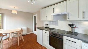 A modern kitchen with white cabinets, a stainless steel range, and a dining area with a table and chairs. - 2 Bed in Hoxne (oc-b45969) (Hoxne)