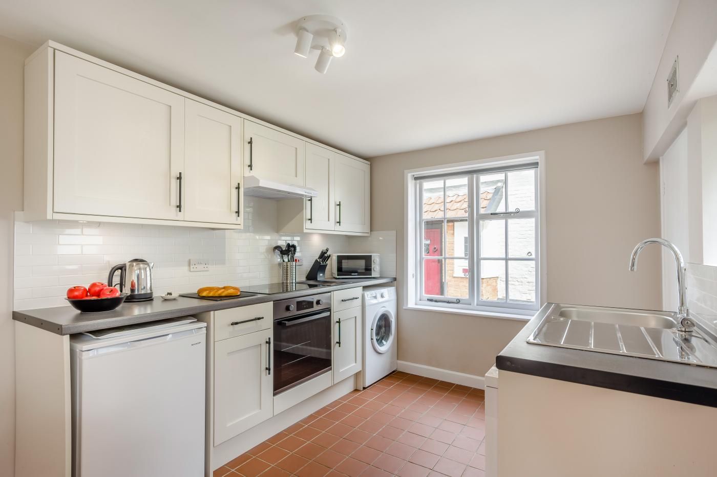 A modern kitchen with white cabinets, a built-in oven, a microwave, and a washing machine.