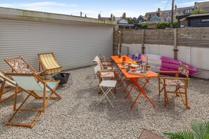 An outdoor patio with a table set for breakfast, surrounded by folding chairs and a kayak. - 4 Bed in Newquay (oc-t45967) (Newquay)