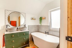 Ein Badezimmer mit freistehender Badewanne, einem grünen Waschtisch mit zwei Becken, einem großen Spiegel und einem Fenster.