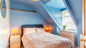 A bedroom with a sloped ceiling, a bed with checkered bedding, bedside lamps, a dresser, and a window with blinds. - 4 Bed in Newquay (oc-t45967) (Newquay)