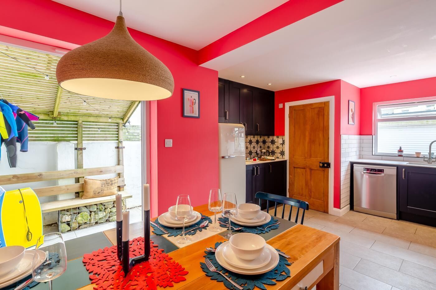 A modern kitchen with red walls, a dining area with a table set for four, and a large hanging light fixture.