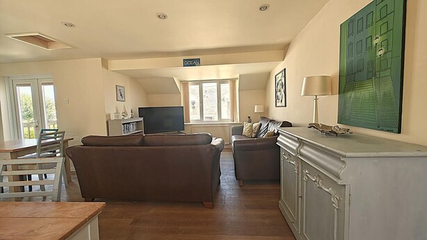 Un salon comprenant un canapé, un téléviseur, un coin repas avec une table et des chaises, ainsi qu’un grand tableau accroché au mur.