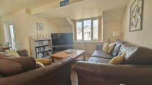 Un salon avec un canapé, une table basse, un téléviseur et une bibliothèque.