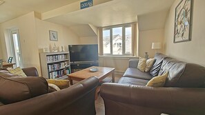 A living room with a sofa, a coffee table, a TV, and a bookshelf. - 2 Bed in Newquay (oc-t45990) (Newquay)