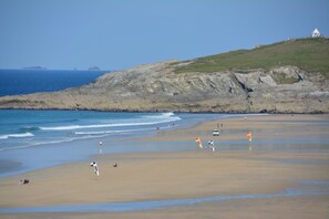 A beach with a rocky cliff and a small white building on top. - 2 Bed in Newquay (oc-t45990) (Newquay)