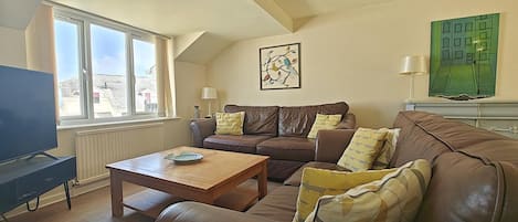 A living room with a brown leather sofa, a wooden coffee table, a television, and a painting on the wall.