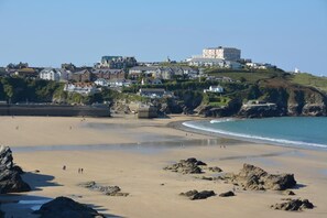 A coastal town with a sandy beach, rocky outcrops, and a hilltop with buildings. - 2 Bed in Newquay (oc-t45990) (Newquay)