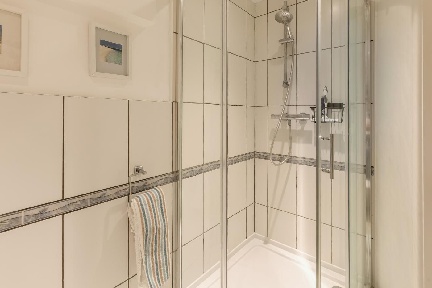 A glass-enclosed shower area with a handheld showerhead and a wall-mounted control panel.
