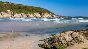 Ein Strand mit Felsen, Wellen und blauem Himmel.