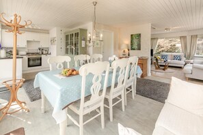 A dining area with a table set for four, surrounded by white chairs, a chandelier, and a view of the kitchen. - 1 Bed in Swanpool (oc-p45941) (Goldenbank)