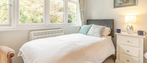 A bedroom with a bed, a bedside table with a lamp, a picture on the wall, and a window with curtains.