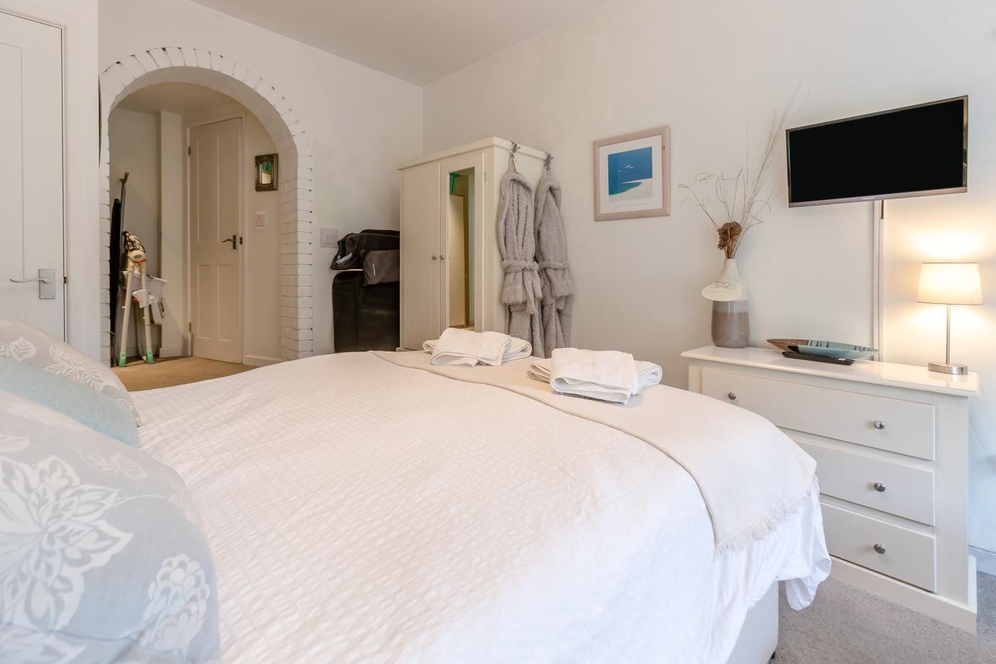 A hotel room with a large bed, a vanity with a mirror, a flat-screen TV, and a framed picture on the wall.