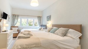 Ein Schlafzimmer mit einem großen Bett, Nachttischen, einem Fenster mit Vorhängen und einem an der Wand montierten Flachbildfernseher.