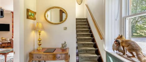 A staircase with a wooden handrail and carpeted steps, a desk with a lamp and a framed picture, and a window with a fox statue.