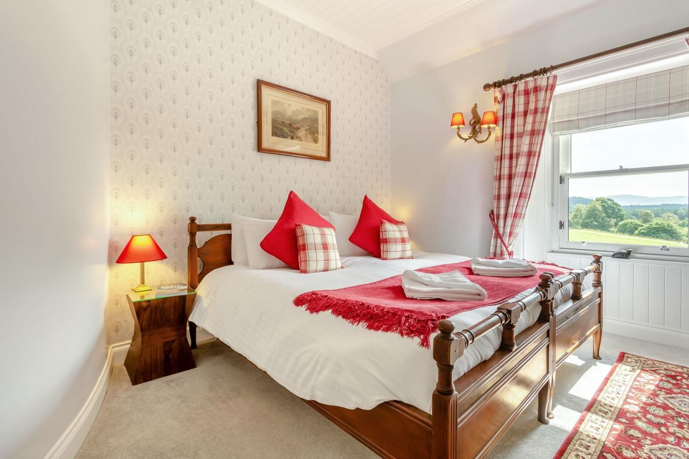 Un lit bien fait, avec une literie rouge et blanche, une lampe de chevet et une fenêtre avec des rideaux.