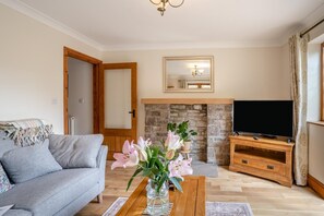 A living room with a sofa, a coffee table with flowers, a TV on a wooden stand, and a stone fireplace.