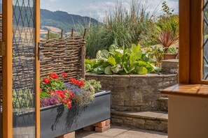 Un balcón con pared de piedra, enrejado de madera y una variedad de plantas y flores en macetas.