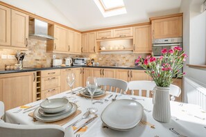 A modern kitchen with wooden cabinets, a dining table set for two, and a vase with flowers.