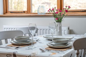 Una mesa de comedor dispuesta con platos, vasos y cubiertos, con un florero sobre la mesa.