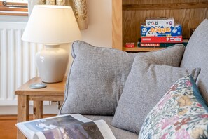 Una sala de estar acogedora con un sofá gris, una mesita de madera con una lámpara y una pila de juegos de mesa.