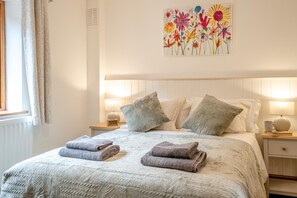 Una cama bien hecha con almohadas, una lámpara de noche y una obra de arte en la pared.