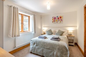 Un dormitorio con una cama, dos mesitas de noche, una ventana con cortinas, un radiador y una lámpara de pared.