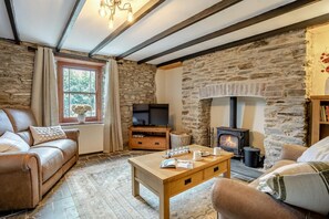 A cozy living room with a stone fireplace, leather sofa, wooden coffee table, and a television. - 2 Bed in Saron (oc-l45978) (Pentre-cwrt)