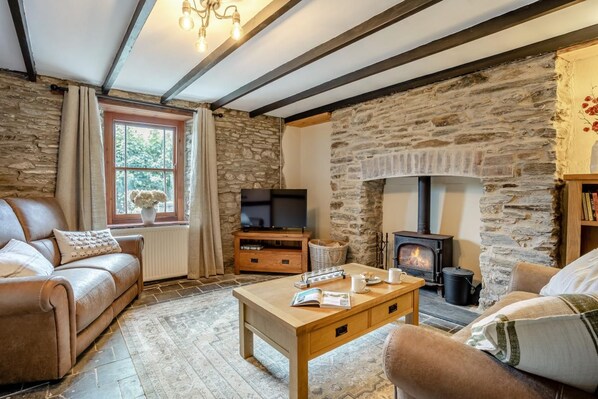 A cozy living room with a stone fireplace, leather sofa, wooden coffee table, and a television.