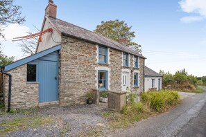 A stone house with a blue door and windows, a gravel driveway, and a rural setting. - 2 Bed in Saron (oc-l45978) (Pentre-cwrt)
