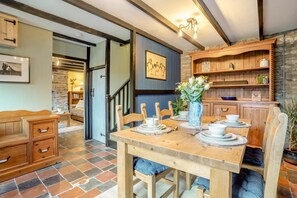 Ein Essbereich mit einem Holztisch, gedeckt für vier Personen, flankiert von Stühlen, und ein Küchenbereich mit Holdekor und einer Steinwand.