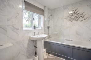 A bathroom with a marble floor, a white sink, a bathtub, and a window with a view of trees.