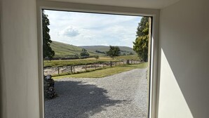 A room with a large window offering a view of a rural landscape with rolling hills, a gravel path, and a stone wall. - 3 Bed in Litton (oc-e45988) (Litton)