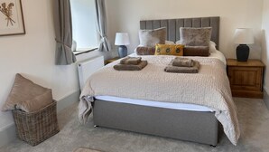 A neatly made bed with a headboard, a bedside table with a lamp, a wicker basket, and a framed picture on the wall. - 3 Bed in Litton (oc-e45988) (Litton)