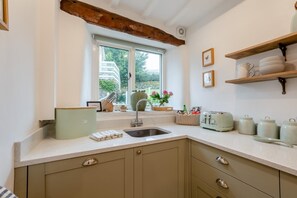 Eine Küche mit Fenster, Holzbalken, einer Spüle, einem Toaster und einem Regal mit Geschirr.