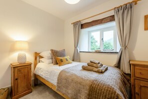 Ein Schlafzimmer mit Bett, Nachttischlampe, einem Fenster mit Vorhängen und einem Holznachttisch.