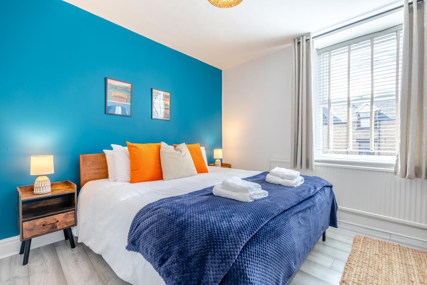 A hotel room with a bed, two bedside tables, a window with curtains, and a blue wall.