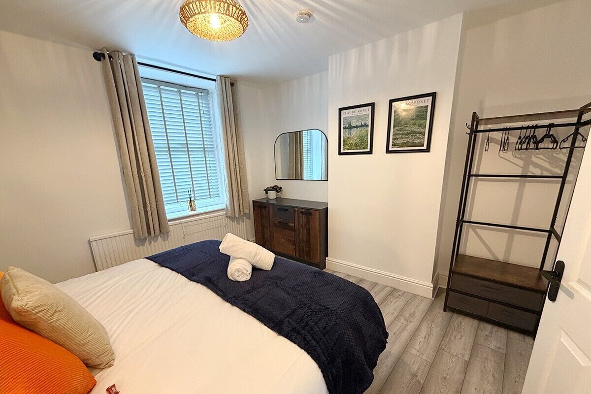 Un dormitorio con cama, cómoda, espejo y perchero.