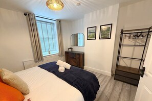 Ein Schlafzimmer mit Bett, Kommode, Spiegel und Kleiderständer.