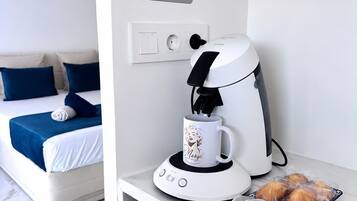 Una habitación de hotel moderna con una cama, una cafetera, una taza y un plato de pasteles.