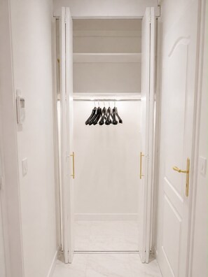 Un couloir avec une porte blanche au fond, un porte-chaussures au-dessus, et un luminaire fixé au mur.