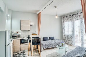 A compact living space with a kitchenette, a dining area with two chairs, a bed with patterned bedding, and a glass coffee table. - Cozy apartment in a quiet neighborhood close to Chios downtown (Chios)