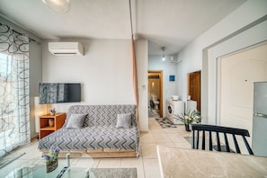 A modern living room with a sofa, TV, and a dining area with a table and chairs. - Cozy apartment in a quiet neighborhood close to Chios downtown (Chios)