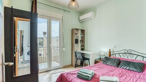 Ein Schlafzimmer mit Bett, Schreibtisch, Stuhl, Kleiderschrank und einer Glastür zu einem Balkon.