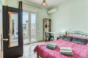Ein Schlafzimmer mit Bett, Schreibtisch, Stuhl, Kleiderschrank und einer Glastür zu einem Balkon.
