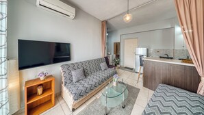Ein modernes Wohnzimmer mit einer Couch, einem Glastisch, einem Flachbildfernseher und einer Küchenzeile mit Kühlschrank und Spüle.